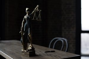 Figurka Pani Sprawiedliwości na drewnianym stole w słabo oświetlonym pomieszczeniu, symbolizująca prawo i sprawiedliwość
