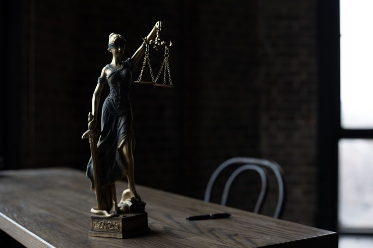 Figurka Pani Sprawiedliwości na drewnianym stole w słabo oświetlonym pomieszczeniu, symbolizująca prawo i sprawiedliwość