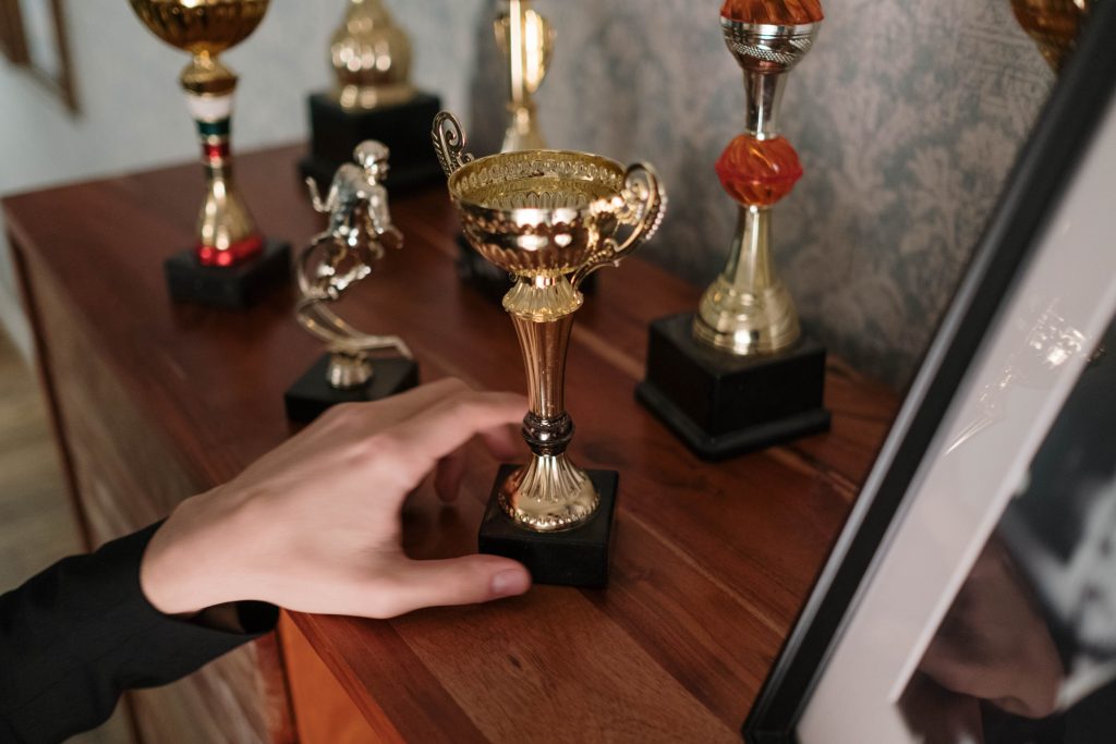 Zbliżenie dłoni sięgającej po błyszczące trofeum na drewnianej półce, symbolizujące sukces