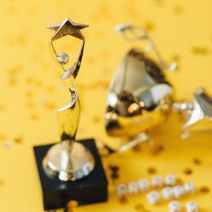 Złoty trofeum w kształcie gwiazdy z konfetti na żółtej powierzchni, symbolizujące sukces i osiągnięcia